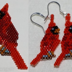 May include: A pair of beaded cardinal earrings with silver hooks. The cardinals are red with black eyes and brown beaks. The earrings are about 2 inches long.