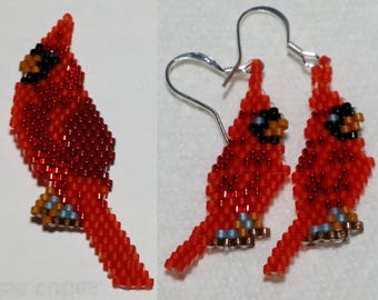 Puede incluir: Un par de pendientes de cardenal hechos con cuentas y con ganchos de plata. Los cardenales son rojos con ojos negros y picos marrones. Los pendientes miden aproximadamente 5 cm de largo.