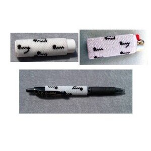 May include: A white pen, eraser, and lighter case with a black, wavy pattern. The pen is a Pilot G-2 07. The lighter case has a red accent. The items are on a gray surface.