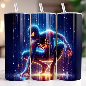 Puede incluir: Tres vasos de acero inoxidable con un gr&aacute;fico colorido de un superh&eacute;roe con un traje azul, rojo y amarillo de pie en una lluvia de luz. El fondo es azul oscuro con rayas blancas de luz.