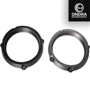May include: Two black and grey speaker rings. The rings are circular with mounting holes and a textured finish. The ONDRA MOTORSPORTS logo is in the upper right corner.
