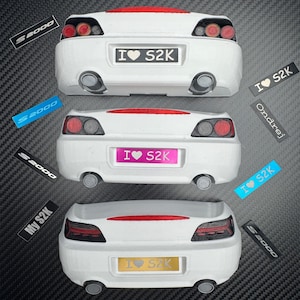 Puede incluir: Tres modelos de coches blancos con luces traseras rojas y el texto "I ♥ S2K" en las matrículas. Cada modelo tiene una matrícula de diferente color. Varias pegatinas "S2000" y "My S2K" están esparcidas alrededor de los coches.