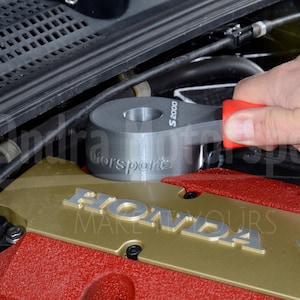 May include: A gray metal wrench with a red handle, labeled "S2000" and "Gorsport", is being used to tighten a bolt on a red and gold Honda engine.