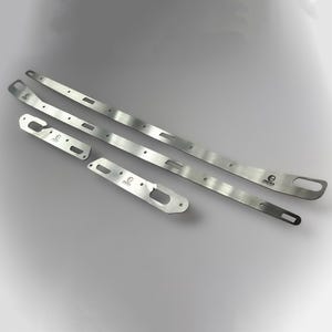 Puede incluir: Cuatro piezas de metal plateado, que incluyen dos tiras largas y delgadas con recortes rectangulares y extremos redondeados, y dos piezas más cortas con aberturas en forma de ojo de cerradura. Las piezas tienen la palabra "ONORA" impresa.