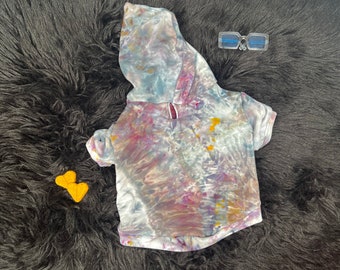 Puede incluir: Una sudadera con capucha tie-dye para mascotas, con un esquema de color azul claro, morado y amarillo. La sudadera tiene un corte holgado y una sensación suave y cómoda.