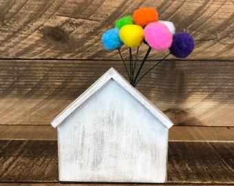 May include: A white wooden house with a distressed finish, with colorful pom-poms attached to the roof, resembling balloons.
