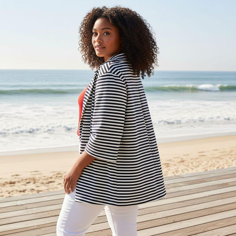 May include: A black and white striped blazer with three-quarter sleeves. The blazer is worn over a red top and white trousers. The background features a beach with the ocean and blue sky.