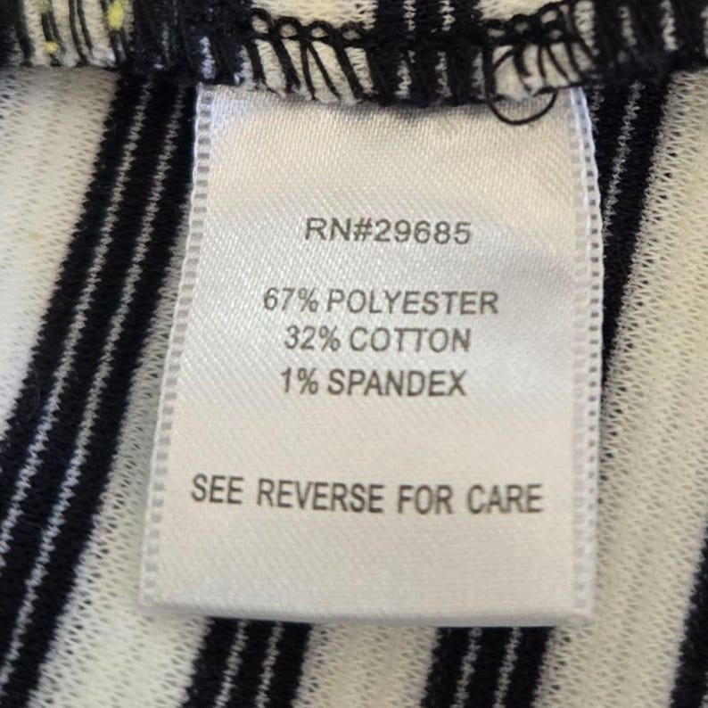 May include: A close-up of a white fabric label with black text. The label displays "RN#29685", and the fabric composition: 67% polyester, 32% cotton, and 1% spandex. The text "SEE REVERSE FOR CARE" is at the bottom.