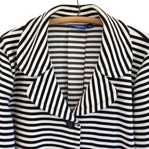 May include: A black and white striped blazer with a notched collar and a single button fastening. The jacket is suspended on a wooden hanger. The stripes are horizontal and evenly spaced.