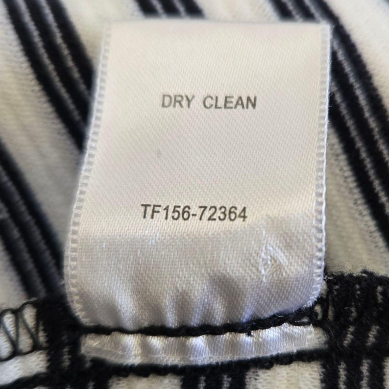 May include: A close-up of a white fabric label with the words "DRY CLEAN" printed in black. Below the text is the number "TF156-72364". The label is attached to a black and white striped fabric.