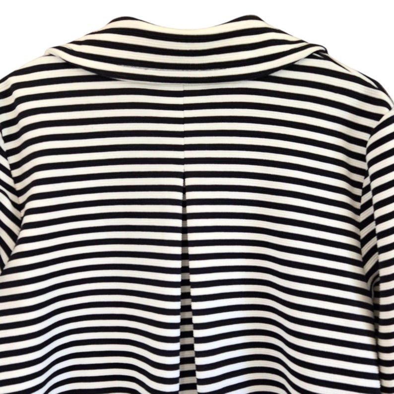 May include: A close-up shot of a black and white striped jacket. The jacket has horizontal stripes and a notched collar. The back of the jacket is visible, showing a split seam detail. The fabric appears to be a medium weight material.