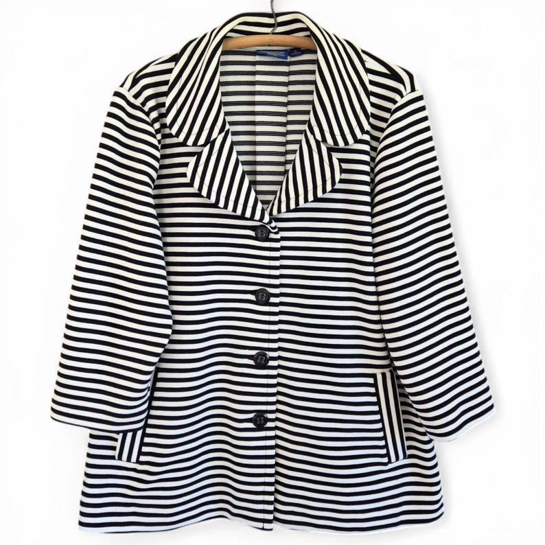 May include: A black and white striped blazer with a notched collar, three-quarter sleeves, and three black buttons. The blazer has a classic design with a tailored fit and two front pockets. The garment is hanging on a wooden hanger.