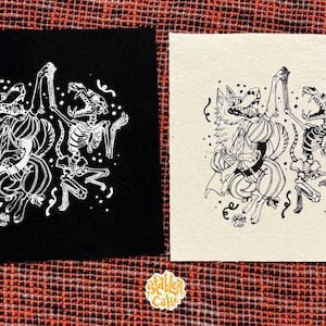May include: Two square patches with a black and off-white background. Each patch features a white illustration of a wolf-like creature and a skeleton dancing together. The patches are on a red and orange plaid surface.