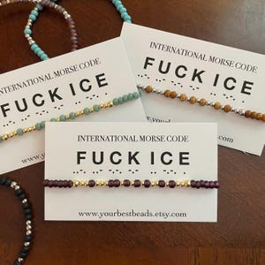May include: Several beaded bracelets with the phrase "FUCK ICE" in International Morse Code are displayed on white cards. The bracelets feature various bead colors, including green, brown, and purple, with gold accents. The Etsy shop URL is visible.