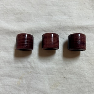 May include: Three cylindrical wooden objects in a deep burgundy colour. The items are evenly spaced and appear polished, with visible wood grain. They are likely decorative or functional, possibly for home decor or crafts.