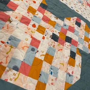 May include: A patchwork quilt with a blue background and a pattern of squares in various colors, including pink, orange, and white. The quilt features a variety of small, colorful designs, including animals, flowers, and geometric shapes.