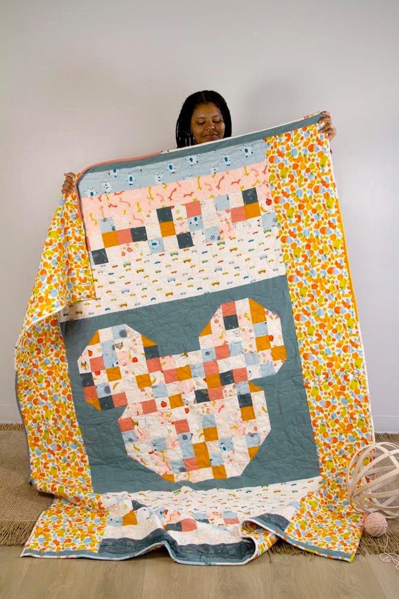 May include: A quilt with a Mickey Mouse design made from colorful patchwork fabric. The quilt is blue, pink, orange, and white. The quilt is folded in half and held by a person.