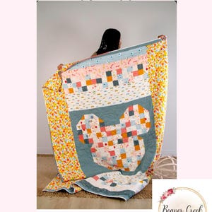 Könnte beinhalten: Eine bunte Patchwork-Decke mit einem großen Mickey-Maus-Kopf-Design in der Mitte. Die Decke ist aus verschiedenen Stoffen in den Farben Rosa, Orange, Gelb, Blau und Weiß gefertigt. Die Decke wird von einer Person gehalten, und der Hintergrund ist eine weiße Wand.