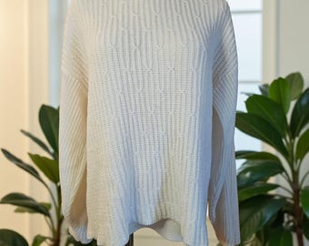 May include: Cream-colored sweater with a textured knit pattern. The sweater has a crew neck and long sleeves. The knit pattern is a repeating design of vertical and horizontal lines. The sweater is displayed on a mannequin.