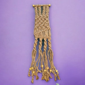 May include: A handcrafted macrame plant hanger made of natural jute rope. The beige-colored hanger features intricate knotting patterns and is adorned with small, yellow wooden beads. The design includes multiple strands for holding a plant pot.