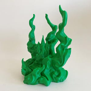May include: A bright green, three-dimensional sculpture depicting stylized, swirling flames or smoke rising from a central point. The object features organic, flowing curves and pointed peaks, creating a dynamic, textured appearance in a solid color.