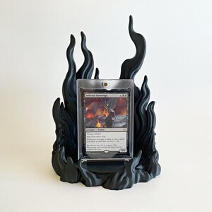 May include: A black display stand shaped like stylized flames holding a clear plastic card protector. Inside the protector is a Magic: The Gathering trading card titled Infernal Sovereign, featuring a demon illustration and game text.