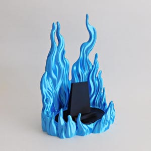 May include: A display stand featuring a central black trapezoidal support mounted on a circular black base, surrounded by a sculpted, metallic blue flame-like structure that rises vertically to create a decorative border around the center.