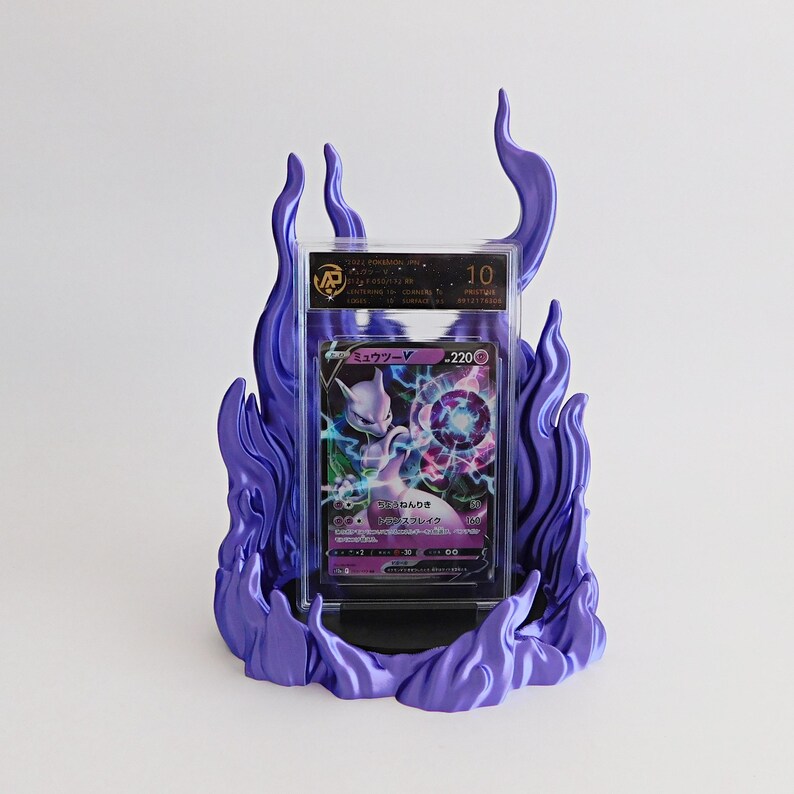 May include: A graded Mewtwo V trading card encased in a clear plastic slab, displayed within a purple flame-shaped stand. The card features a purple and black color scheme with Japanese text and a 220 HP value. The slab displays a grade of 10.