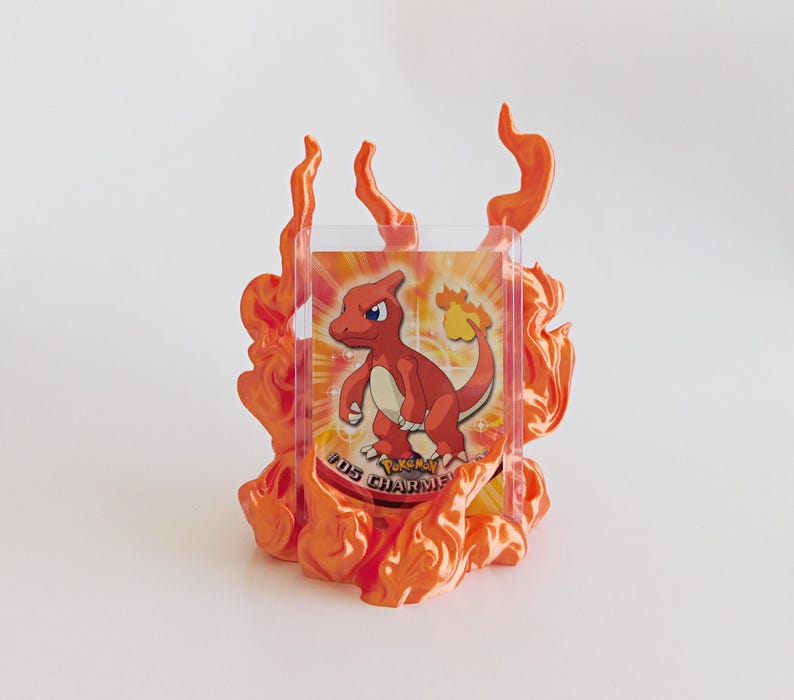 May include: A trading card featuring the red Pokemon Charmeleon with the text #05 CHARMELEON, encased in a clear plastic protective sleeve, held within a three-dimensional orange flame-shaped display stand with a glossy finish.