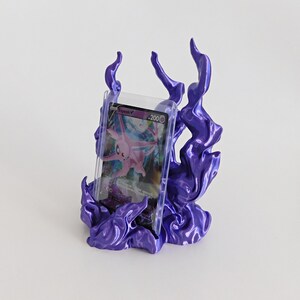 May include: A purple display stand shaped like stylized flames holding a clear plastic protective case containing a pink Espeon V trading card with 200 HP. The stand features a glossy finish and organic, swirling flame-like structures.