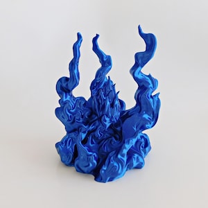 May include: A metallic blue figurine depicting a central figure surrounded by swirling, flame-like structures. The object features a glossy, reflective finish with intricate, sculpted details that mimic the appearance of rising smoke or fire.