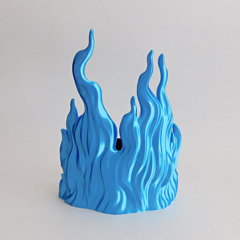 May include: A bright blue decorative object shaped like stylized flames with a smooth, glossy finish. The structure features multiple vertical, undulating peaks of varying heights that create a continuous, wave-like pattern around the perimeter.
