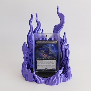 May include: A purple flame-shaped display stand holding a clear plastic protective case containing a Demon of Fate's Design trading card. The stand features sculpted, swirling flame details that surround the card on all sides.