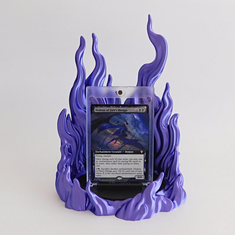 May include: A purple flame-shaped display stand holding a clear plastic protective case containing a Demon of Fate's Design trading card. The stand features sculpted, swirling flame details that surround the card on all sides.