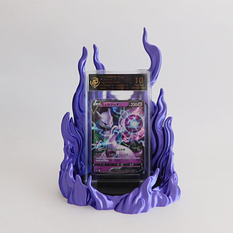 May include: A graded Mewtwo V trading card encased in a clear plastic slab, displayed within a purple flame-shaped stand. The card features Japanese text, a purple color scheme, and a 220 HP rating. The slab label shows a grade of 10.