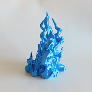 May include: A bright blue, three-dimensional sculpture shaped like stylized, upward-reaching flames. The object features a glossy, metallic finish with smooth, flowing curves and pointed tips that mimic the appearance of fire in a vibrant cyan hue.