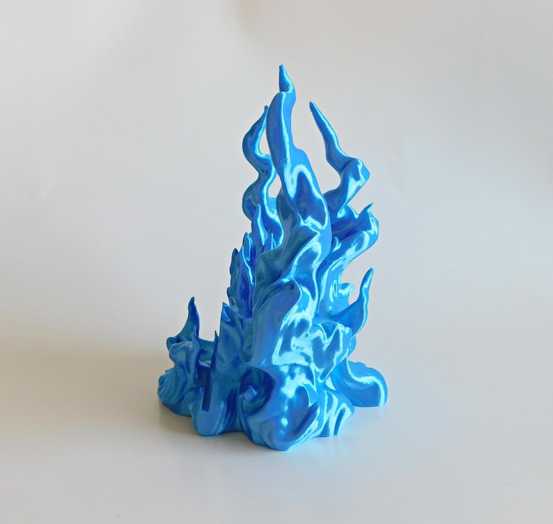 May include: A bright blue, three-dimensional sculpture shaped like stylized, upward-reaching flames. The object features a glossy, metallic finish with smooth, flowing curves and pointed tips that mimic the appearance of fire in a vibrant cyan hue.