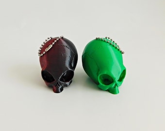 May include: Two small alien skull keychains, one is black and red, the other is green. Both have a silver chain attached.