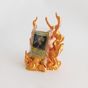 May include: A metallic orange display stand shaped like stylized flames, holding a Japanese trading card encased in a clear plastic protective sleeve. The card features a yellow creature illustration and Japanese text including HP70.