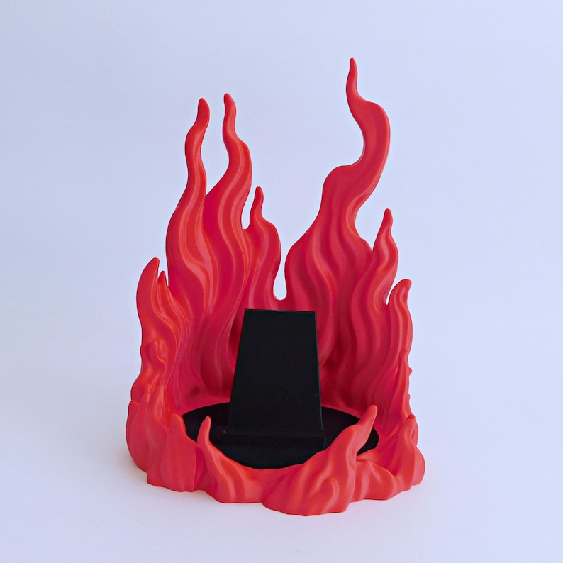 May include: A display stand featuring a sculpted red flame design surrounding a central black, trapezoidal pedestal. The structure is composed of multiple vertical, wavy flame-like protrusions that rise from a circular base, providing a backdrop for items.