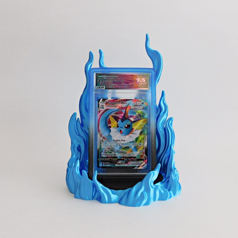 May include: A graded Vaporeon VMAX trading card encased in a clear plastic slab, displayed within a bright blue, flame-shaped stand. The card features a blue creature illustration, the text Vaporeon VMAX, and a DGA 9.5 grade label at the top.