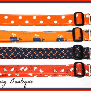May include: Four fabric straps with different patterns and metal clips. The straps are orange with white polka dots, orange with blue whales, navy blue with orange polka dots, and red with white birds. The straps are all about 1 inch wide and have a black buckle.