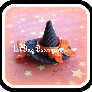 May include: A black witch hat with an orange ribbon and a rhinestone accent. The hat is on a pink background with white stars.