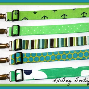 May include: Five different green and blue fabric straps with silver clips. The straps have various patterns including anchors, polka dots, stripes, and flowers. The straps are labeled "LiliBug Boutique".