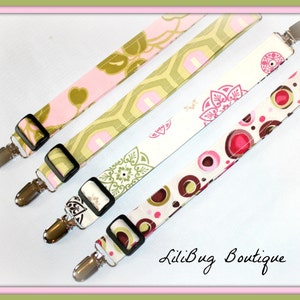 May include: Four fabric straps with silver clips and different patterns. The patterns include pink and green floral, green and white geometric, white with pink and green floral, and white with pink and brown circles. The straps are arranged in a diagonal line with the text "LiliBug Boutique" at the bottom.
