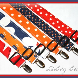 May include: Five colorful fabric straps with metal clips. The straps feature different patterns, including orange and white polka dots, navy blue and white polka dots, red and white polka dots, and a white background with navy blue and orange whales. The straps are all attached to silver metal clips.