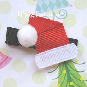 Peut inclure: Une barrette de cheveux en forme de chapeau de Père Noël rouge et blanc avec un pompon blanc. La barrette est noire et a une bande blanche.