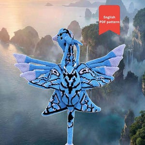 May include: A blue and black crocheted bird with outstretched wings, featuring intricate patterns. The bird has a long neck and tail, with a white and light blue color scheme. The image includes a red rectangle with the text "English PDF pattern".