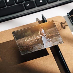 May include: A white business card with a brown background image of a couple in a field. The text "Olivia Wilson Photography" is printed in white on the card.