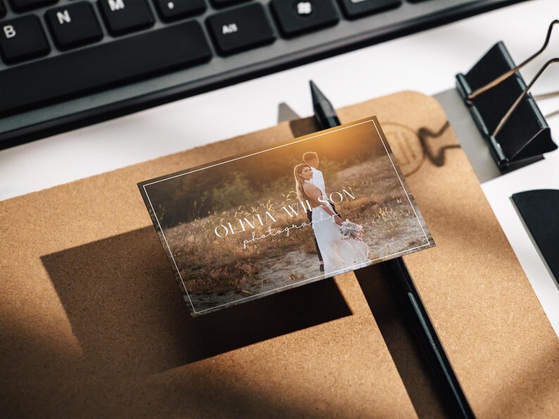 May include: A white business card with a brown background image of a couple in a field. The text "Olivia Wilson Photography" is printed in white on the card.